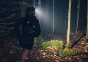Löpare med pannlampa springer på en mörk, mossig skogsstig