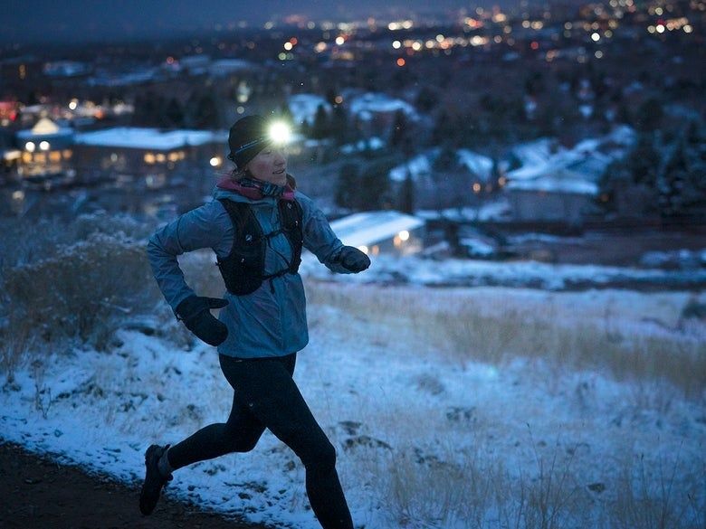 Löpare med pannlampa springer på en snötäckt stig i skymningen